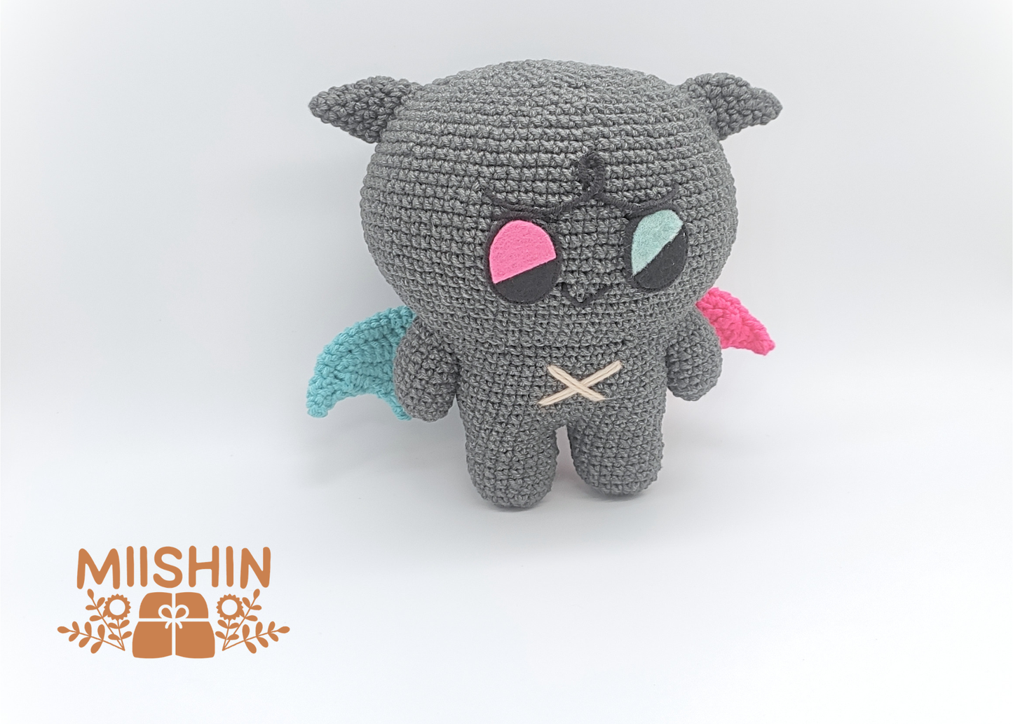 Vista lateral del amigurumi Kkamyo mostrando alas bicolor, azul y rosa.