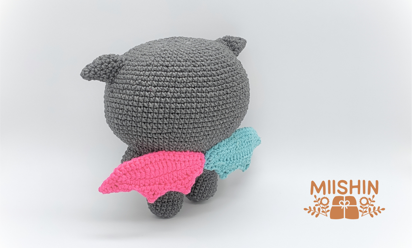 Vista trasera del amigurumi Kkamyo mostrando el peluche de pie y las alas de colores.